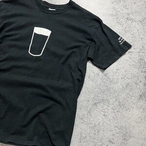 May include: Black t-shirt featuring a white outline of a pint glass. The shirt has a crew neck and short sleeves. The text "NOT BLACK MAKES SENSE" is printed on the sleeve.