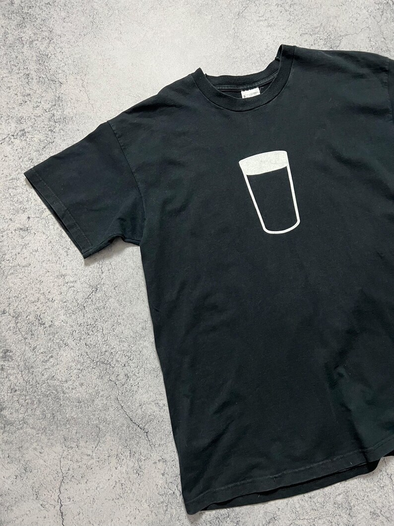 May include: Black t-shirt featuring a white outline of a pint glass. The graphic is centered on the chest. The shirt has short sleeves and a crew neck. The fabric appears to be cotton.