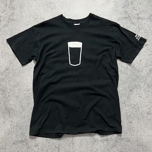 May include: Black t-shirt featuring a white outline of a pint glass. The shirt has short sleeves and a crew neck. The text on the sleeve is blurry.