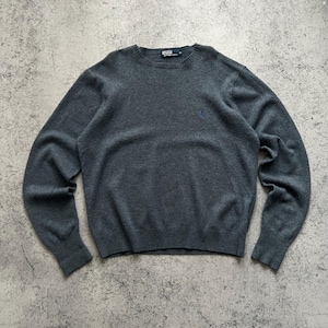 May include: A dark grey crew neck sweater with a small blue logo on the chest. The sweater features ribbed cuffs and hem. The brand label is visible at the back of the neck. A classic sweater for everyday wear.