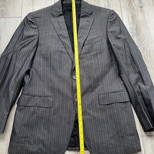 May include: A charcoal gray pinstriped blazer with a notched lapel, two front buttons, and two flap pockets. A yellow measuring tape is placed vertically over the center, showing a length of approximately 30 inches from collar to hem.