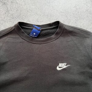 May include: Black crew neck sweatshirt with the Nike logo embroidered in white on the chest. The sweatshirt has a tag attached near the collar. The fabric appears to be a soft, comfortable material.