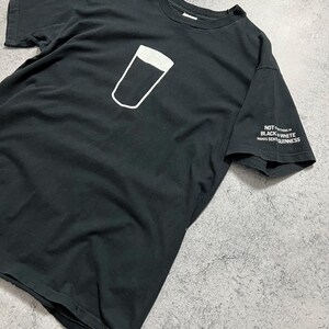 May include: Black t-shirt featuring a white outline of a pint glass with a dark fill. The sleeve has the text "NOT EVERYTHING IN BLACK & WHITE MAKES SENSE GUINNESS".
