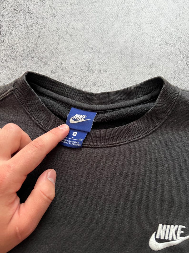 May include: Black crew neck sweatshirt with the Nike logo embroidered in white on the chest and a blue tag at the collar. The tag has the Nike logo and size information. The sweatshirt is a size small.