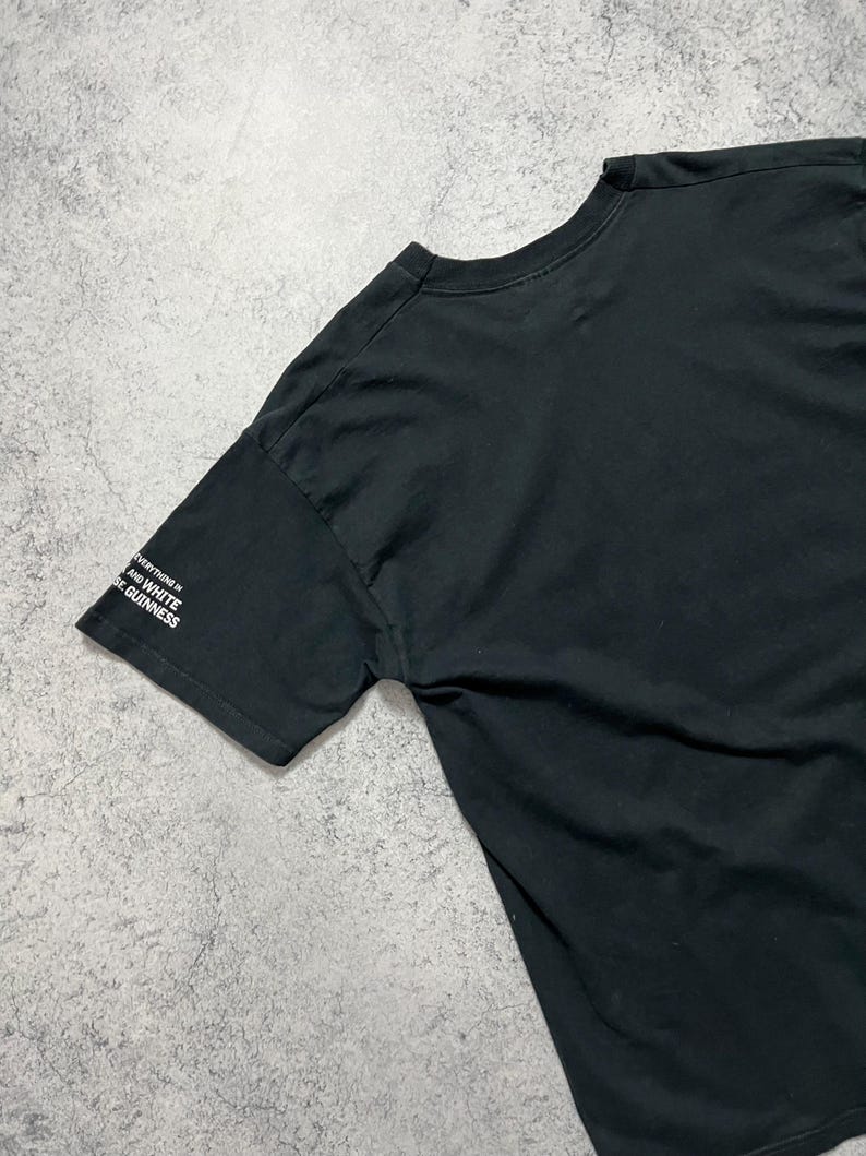 May include: Black t-shirt with the text "Everything is black and white, like Guinness" printed in white on the left sleeve. The shirt is made of a soft material.
