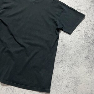 May include: A black crew neck t-shirt. The short-sleeved shirt is made of a soft material and is slightly wrinkled. The shirt is displayed on a gray and white textured surface.