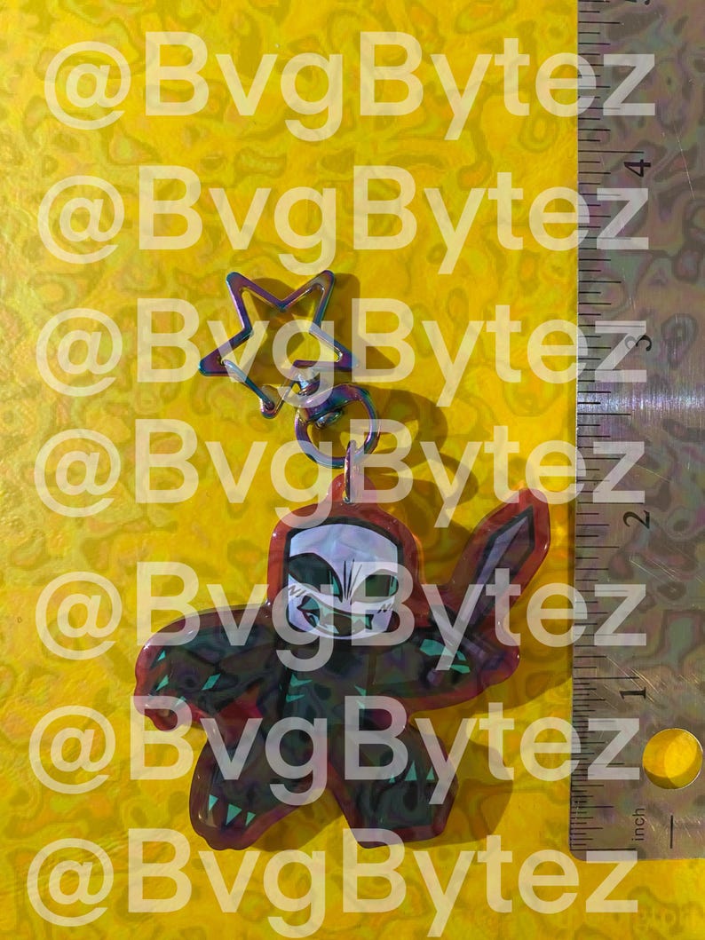 May include: A keychain with a star-shaped charm and a pendant featuring a skull design. The pendant is red and black with green accents. The background is yellow with the text "@BvgBytez".
