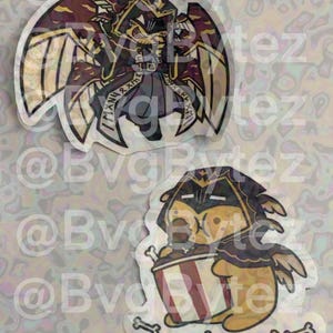 May include: Two die-cut stickers featuring stylized characters. The top sticker shows a winged figure in dark red and gold armor with a halo. The bottom sticker depicts a yellow creature in a dark hood eating from a red and white striped bucket.