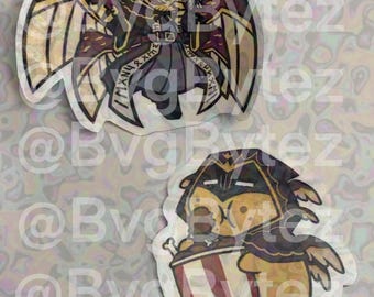 May include: Two die-cut stickers featuring stylized characters. The top sticker shows a winged figure in dark red and gold armor with a halo. The bottom sticker depicts a yellow creature in a dark hood eating from a red and white striped bucket.