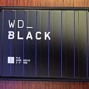 May include: Black WD_BLACK P10 Game Drive 2.5" HDD. The external hard drive has a black case with vertical lines and blue accents. The WD_BLACK logo is in white, along with the P10 Game Drive information.