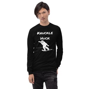Op de afbeelding: Zwart shirt met lange mouwen met de tekst "KNUCKLE HUCK" boven een witte afbeelding van een snowboarder. De snowboarder draagt een helm en is in beweging. Het shirt is gemaakt van een zacht materiaal.