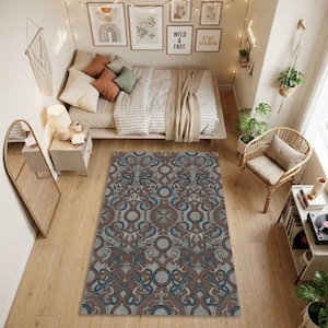 May include: A rectangular area rug featuring a repeating intricate pattern of intertwined blue and rust-colored lines on a light gray background, accented by circular motifs throughout the design, laid flat on a light-colored wooden floor.
