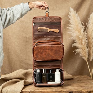 May include: A brown faux leather hanging toiletry bag with a top hook, a mesh zippered pocket containing a wooden comb, a central zippered compartment, and a bottom clear plastic pocket holding four assorted bottles of personal care products.