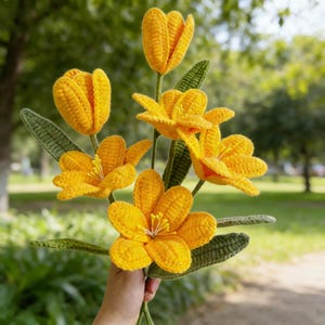 Può includere: Un bouquet di fiori gialli all'uncinetto fatti a mano con foglie verdi. I fiori hanno petali dettagliati e sono tenuti insieme da steli verdi. Il lavoro all'uncinetto è visibile, mostrando la consistenza e l'artigianalità della composizione floreale.