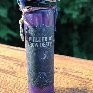 May include: A purple glass bottle with a dark blue wax seal. The label reads "Philter of Drow Destiny" with a crescent moon and a woman's face. The bottle is sealed with a dark blue wax and a silver charm.