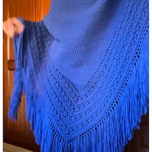 Puede incluir: Un chal azul vibrante con borde de flecos. El chal presenta un diseño calado detallado en los bordes y un centro de punto liso. La flecos añade un elemento decorativo a este cómodo accesorio.