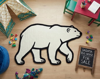 Può includere: Un tappeto bianco a forma di orso polare con bordi neri. Sono visibili anche un pouf blu, un tavolino rosso con sedie verdi e una lavagna con la scritta "SAQUIYA RUG HOUSE FOR SALE".
