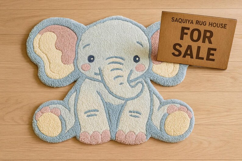 May include: A light blue elephant-shaped rug with pink and yellow accents. The rug has a cartoon-like design and is made of a soft, textured material. A wooden sign that says "FOR SALE" is next to the rug.