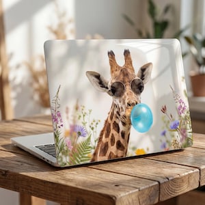 Könnte beinhalten: Laptop mit einem skurrilen Design, das eine Giraffe mit Sonnenbrille und einer blauen Kaugummiblase zeigt. Die Giraffe ist vor einem Hintergrund aus Wildblumen platziert. Der Laptop steht auf einem Holztisch.