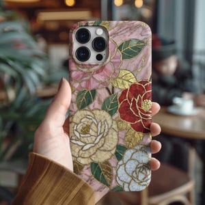 Könnte beinhalten: Eine rosa Handyhülle mit einem floralen Mosaikdesign. Die Hülle zeigt Rosen in Rosa-, Rot- und Weißtönen mit goldenen Akzenten und grünen Blättern. Die Hülle hat eine marmorähnliche Textur.