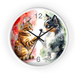 Könnte beinhalten: Weiße runde Wanduhr mit einer Aquarellillustration einer Katze und eines Hundes. Die Katze ist orange und der Hund ist schwarz, weiß und braun. Die Uhr hat schwarze Zeiger und einen weißen Rand. Der Hintergrund ist rot und grün.