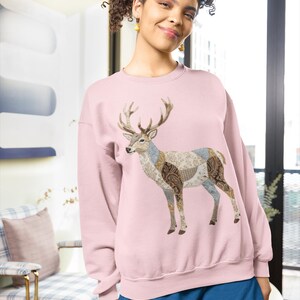 Könnte beinhalten: Hellrosa Sweatshirt mit einem Hirschdesign mit gemusterten Patches in Braun, Blau und Weiß. Der Hirsch hat große Hörner. Die Person trägt blaue Shorts.