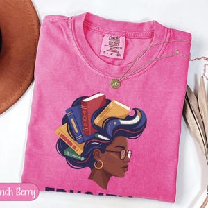 Pink t-shirt with a graphic of a woman with books for hair, wearing glasses.
