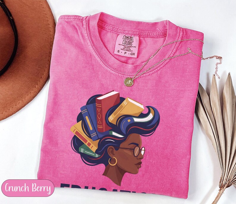Pink t-shirt with a graphic of a woman with books for hair, wearing glasses.