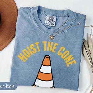 Blue t-shirt with "HOIST THE CONE" text and traffic cone graphic.
