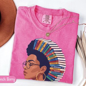 Pink t-shirt with graphic of woman with books for hair, listing subjects.