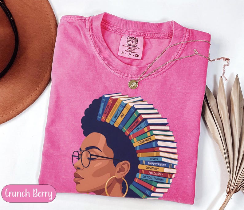 Pink t-shirt with graphic of woman with books for hair, listing subjects.