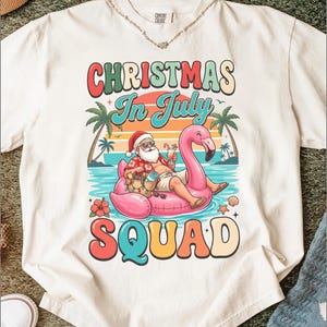 May include: An off-white t-shirt featuring a graphic of Santa Claus wearing sunglasses and a floral shirt while floating on a pink flamingo pool float. The text reads CHRISTMAS In July SQUAD, surrounded by palm trees, a sunset, and ocean waves.