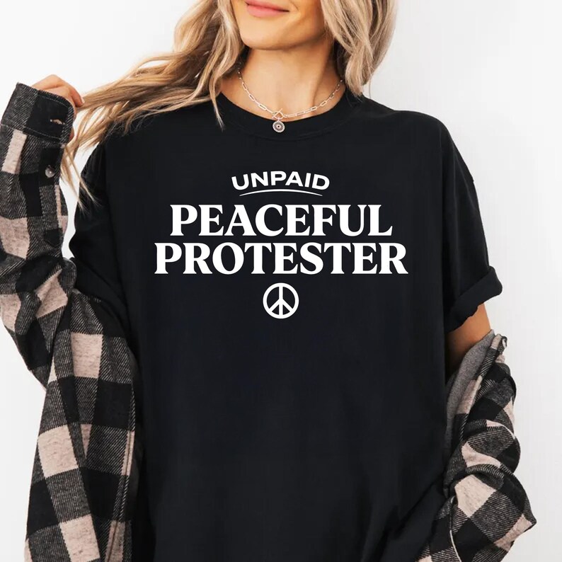 Black t-shirt with white text "UNPAID PEACEFUL PROTESTER" and a peace symbol.
