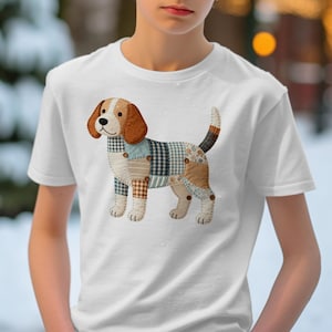 May include: White t-shirt featuring a patchwork beagle design. The dog illustration has brown, tan, blue, and black plaid and solid patches. The beagle has brown ears and a striped tail. The shirt is worn by a person.