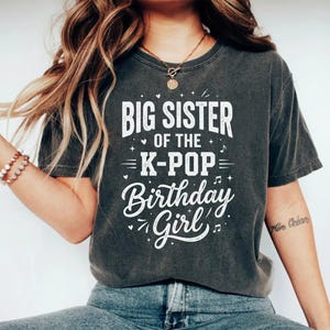Könnte beinhalten: Dunkelgraues T-Shirt mit dem weißen Text "BIG SISTER of the K-POP Birthday Girl". Das Shirt hat einen Vintage-Look. Der Text ist mit Herzen und Noten gestaltet.