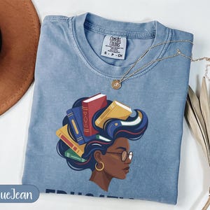 Blue t-shirt with woman's head adorned with books, gold necklace.