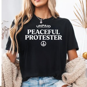 Black t-shirt with "UNPAID PEACEFUL PROTESTER" and peace symbol.