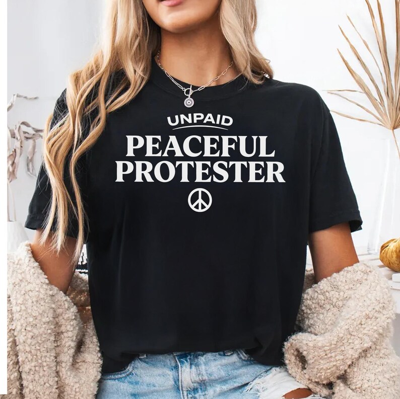Black t-shirt with "UNPAID PEACEFUL PROTESTER" and peace symbol.
