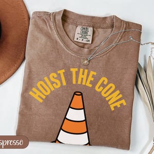 Brown t-shirt with "HOIST THE CONE" graphic and traffic cone.