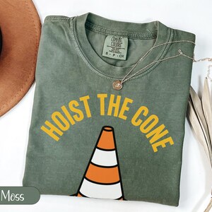 Green t-shirt with "HOIST THE CONE" text and traffic cone graphic.