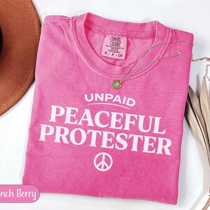 Pink t-shirt with "UNPAID PEACEFUL PROTESTER" and peace symbol.