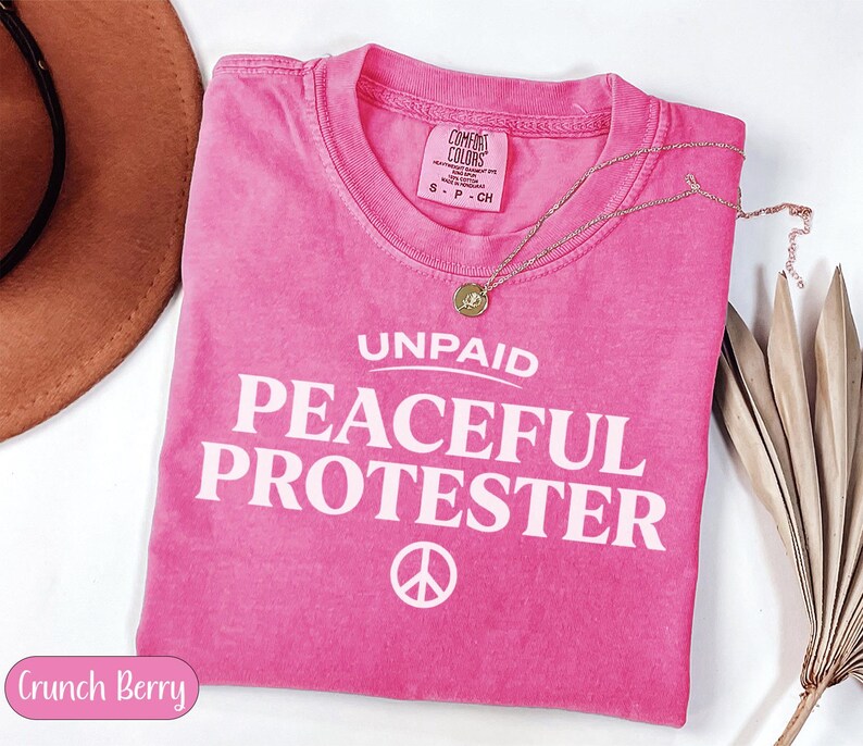 Pink t-shirt with "UNPAID PEACEFUL PROTESTER" and peace symbol.