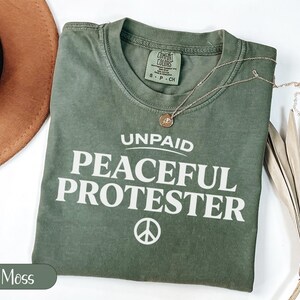 Green t-shirt with "Unpaid Peaceful Protester" graphic and peace symbol.