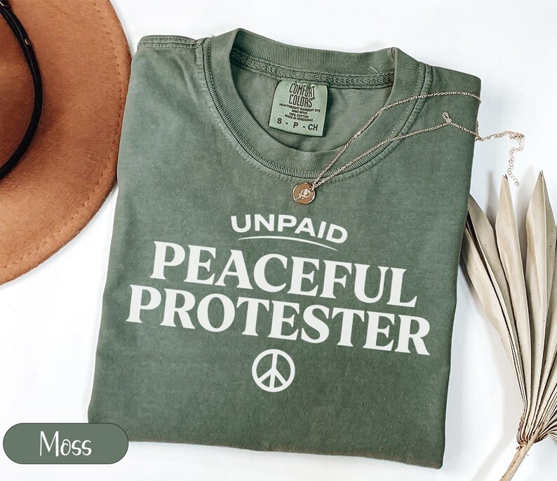 Green t-shirt with "Unpaid Peaceful Protester" graphic and peace symbol.