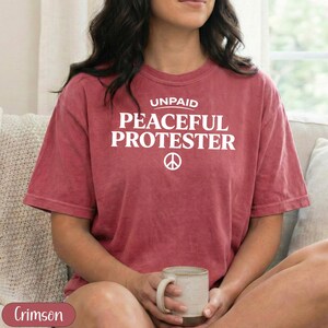 Crimson t-shirt with "Unpaid Peaceful Protester" and peace symbol.
