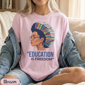Pink t-shirt with graphic of woman with books on head, "EDUCATION IS FREEDOM" text.