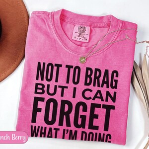 Pink Comfort Colors t-shirt with "NOT TO BRAG BUT I CAN FORGET WHAT I'M DOING" text.