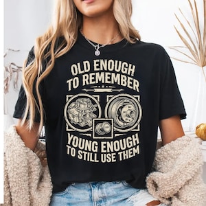 May include: Black t-shirt with the text "OLD ENOUGH TO REMEMBER YOUNG ENOUGH TO STILL USE THEM". The shirt features illustrations of car parts, including a carburetor and a brake drum. The word "CHOKE" is also visible.