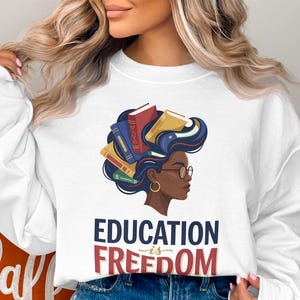 White sweatshirt with "Education is Freedom" text and illustration of woman with books in hair.