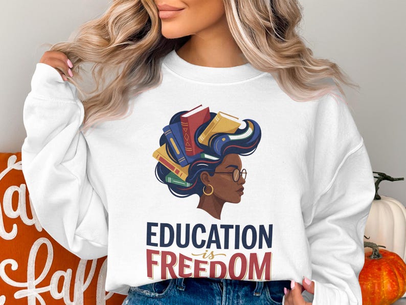 White sweatshirt with "Education is Freedom" text and illustration of woman with books in hair.